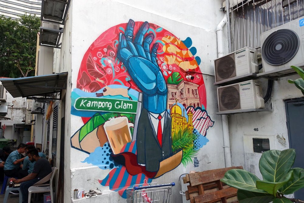 Kampong Glam mural by Zero features a suit-wearing person with a blue hand for a face done in signature Zero-style, and features prominent local icons like food wrapped in banana leaves, teh tarik, Sultan Mosque and the Malay Heritage Centre in the background