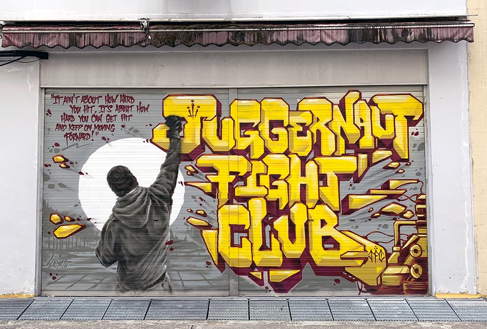 Juggernaut Fight Club Mural by Slacsatu has the club's name in large yellow graffiti-style font and a shot of a man from behind punching upwards. The quote is in the top left corner in red lettering.