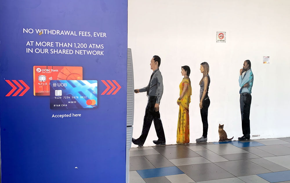 The artwork is on the wall and uses perspective to look like the people are using the ATM