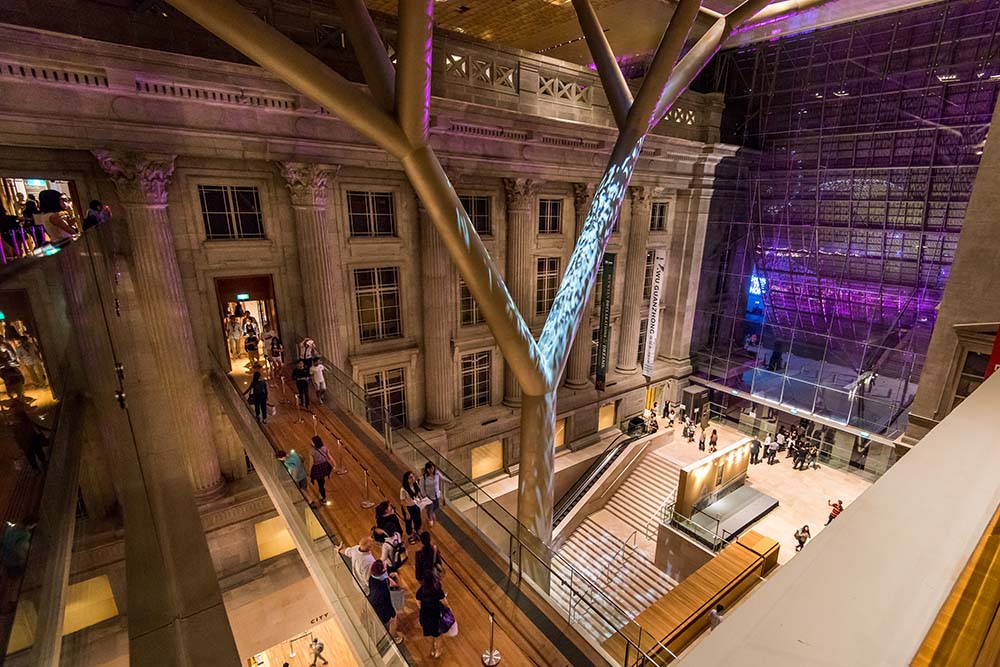 Top down view of large covered atrium with pillars and a stone building facade in the background